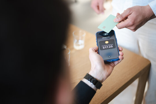 A person holds a phone to make a contactless payment with a card. The transaction is for $17.25 at Grapner's Greenhouse.