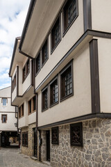 Naklejka premium Traditional Ohrid architecture featuring rough stone foundations, jettied upper floors, smooth light-colored plaster walls, and dark wooden window frames along a narrow urban cobblestone alley.