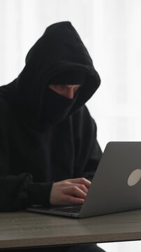 A scammer in a black mask.
A hacker hacks a laptop to obtain digital information.
