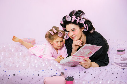 Moscow, Russia, 08.02.2026 Woman and daughter with hair rollers and eye patches read book at home. Mother daughter moment for Mother Day. Family relationship concept.