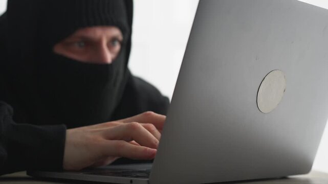 A man with his face covered hacks a server on a laptop.
The hacker uses the laptop for a scam.
Online fraud