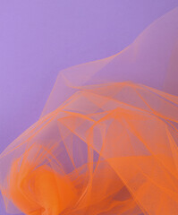 Bright orange tulle fabric on purple background.  Abstract transparent material curve wave.