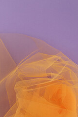 Bright orange tulle fabric on purple background.  Abstract transparent material curve wave.