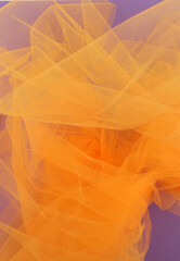 Bright orange tulle fabric on purple background.  Abstract transparent material curve wave.