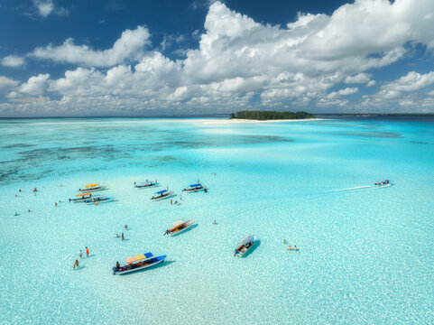 Aerial view of colorful boats in turquoise sea, blue sky with clouds near Mnemba Island, Zanzibar, Tanzania. Crystal clear water, yachts, tropical summer landscape, top drone view. Travel destination