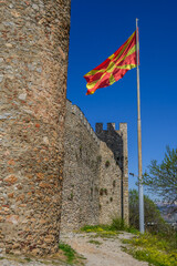 A winding dirt path leads along the ancient stone walls of Samuel's Fortress, crowned by a waving Macedonian flag under clear daylight in Ohrid, North Macedonia. © Danica Chang