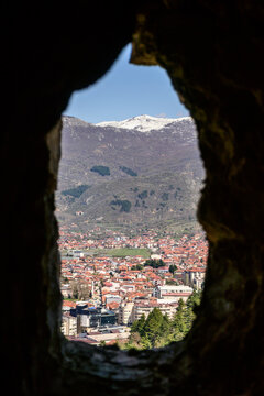 Through an ancient arrow slit window of Samuel's Fortress, Ohrid's red-roofed houses and distant snow-capped mountains are perfectly framed on a bright day.