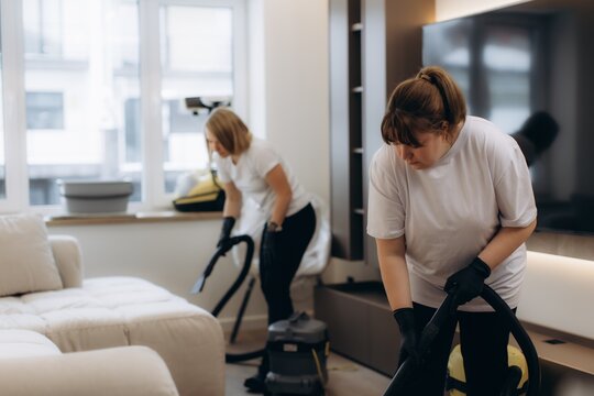 Professional cleaning team vacuuming upholstered furniture in living room