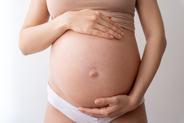 Closeup of impersonal woman, future mother touching naked tummy belly at third trimester showing love, care to baby standing at wall. Pregnant, eco, prenatal maternity, waiting motherhood. Isolated