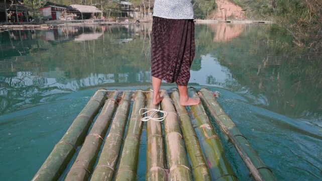 A woman poles a bamboo raft across a river in Hang Than Lim, Yen Minh, Ha Giang, Vietnam. She is transporting tourists the river in Ha Giang.