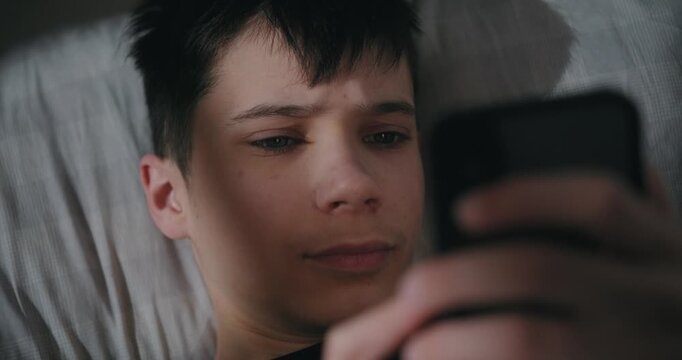 Teenage boy using a smartphone while lying in bed at night.