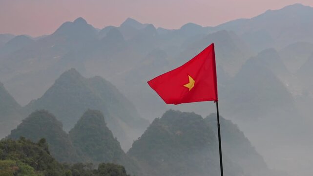 A Vietnamese flag waves in the wind, symbolizing national pride and identity, set against the backdrop of the misty mountains in Yen Minh, Ha Giang, Vietnam.