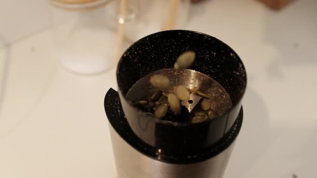 Close-up of green pumpkin seeds being ground into a fine powder or meal. This footage highlights healthy superfood preparation, organic nutrition, vegan protein sources, and the texture of raw pumpkin