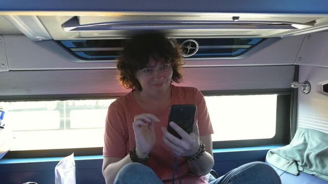 Sleeper Bus Traveler In Bus Berth Tapping Phone, Bright Daylight Through Window, Casual Passenger Engaged With Messaging App, Headphones On, Itinerary Visible, Urban Stop Approaching, Upbeat
