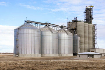 Minimal rural landscape, gray concrete grain elevator built among agricultural fields, cloudy sky, peaceful silent spring countryside and industry. © Saeedatun