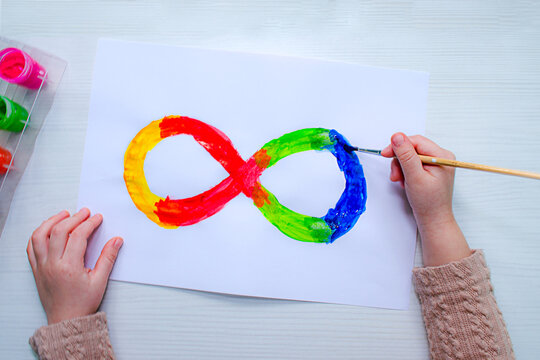 Top view of children&rsquo;s hands painting an infinity symbol in rainbow colors. Creative activity supports child development, fine motor skills, imagination, represents autism awareness neurodiversity.