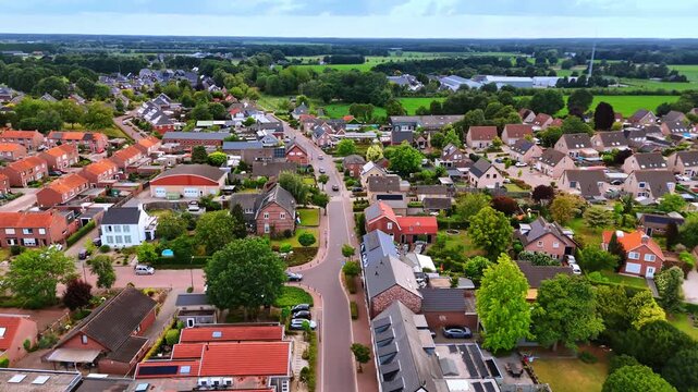 Aerial view of a T-junction in a Dutch residential suburb. A clear view of a road junction surrounded by houses with red roofs, green trees, and private parked cars.