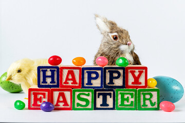 happy Easter in wood blocks with jelly beans colored eggs yellow chick and brown bunny on white background