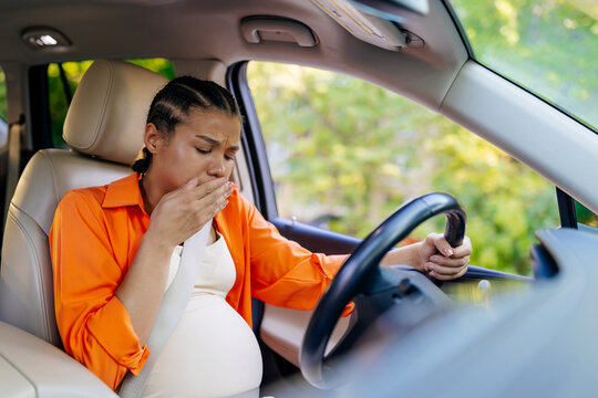 Young black pregnant woman covering mouth while driving car, feeling nausea. African american mother experiencing morning sickness during daily travel