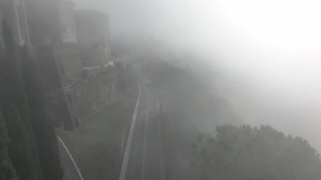 Moody cinematic drone flight above an ancient Italian town covered in dense fog. Historic rooftops barely visible through thick mist, creating a dramatic and atmospheric landscape.