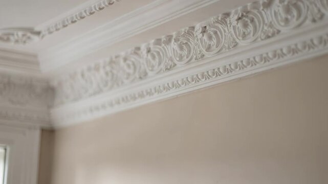 Medium shot of intricate crown molding highlighting its ornate patterns sharp focus on detail with soft blurred inn interior in the background.