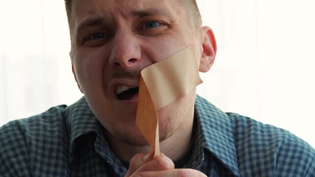 Censorship and silence.
A man removes adhesive tape from his face.
Censorship of speech.