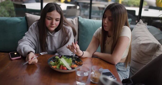 Two Teenage Girls Enjoying a Healthy Salad and Sharing a Laugh at a Cafe