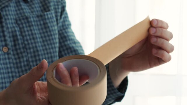A close-up of sticky tape in a man's hands.
A close-up of brown sticky tape.