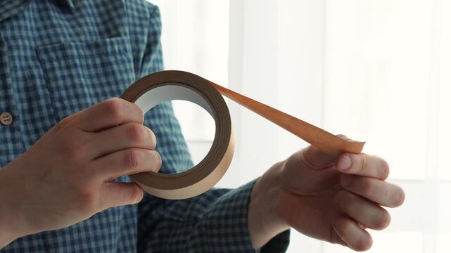 A close-up of sticky tape in a man's hands.
A close-up of brown sticky tape.