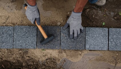 Person laying gray paving stones with rubber mallet outdoors construction hands