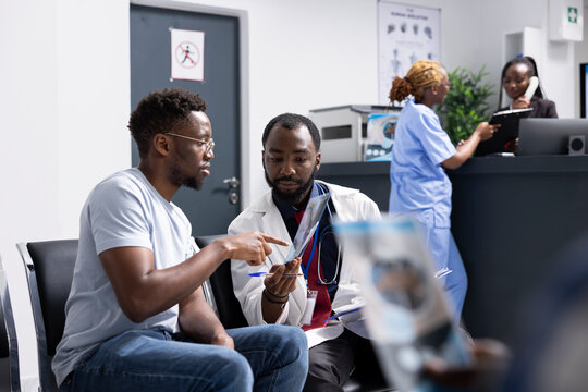 Focused conversation unfolds as doctor reviews xray scan with black male patient during clinic visit. Physician explains findings clearly, assisting man with next steps and treatment options.