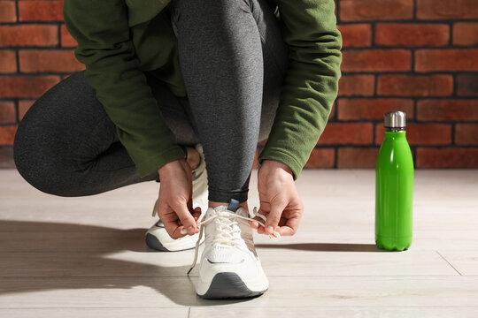 Woman tying shoelace of white sneaker indoors, closeup
