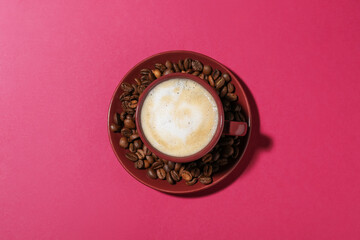 Cup of aromatic coffee and beans on crimson background, top view