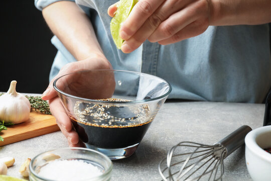 Woman squeezing lime juice into bowl with soy sauce for marinade at gray textured table, closeup