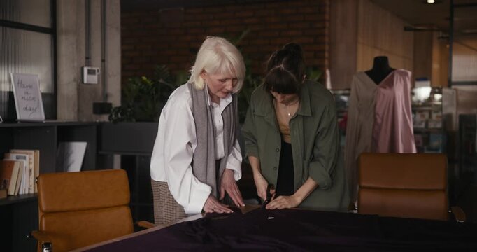 Two women work closely together, creating beautiful garments in a cozy sewing studio filled with fabric and creativity