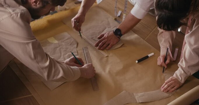 Hands craft clothing patterns with tools, highlighting the art of garment design in a collaborative space