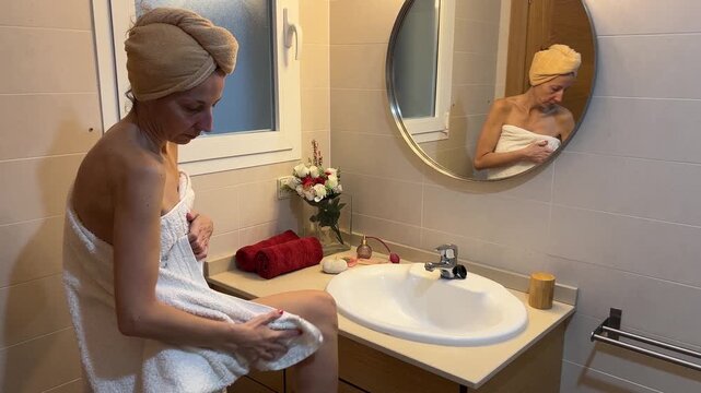 Mujer sec&aacute;ndose con toalla frente al espejo del lavabo tocador