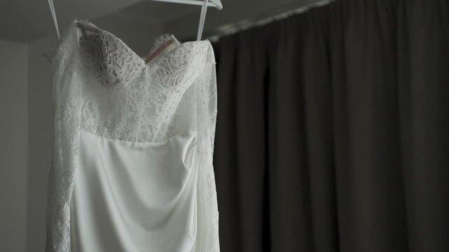A white wedding dress hangs on a chandelier by the window