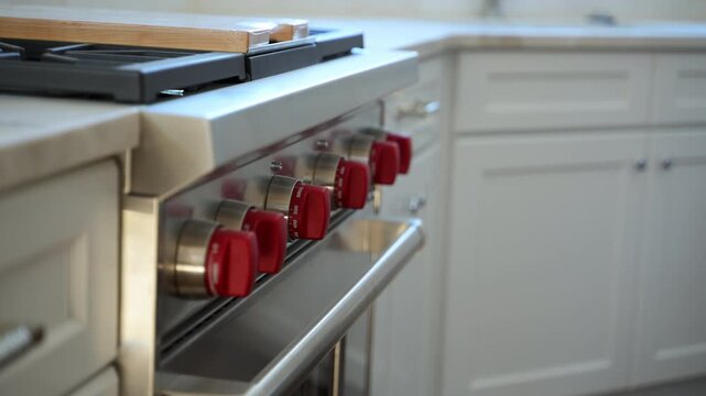 Close-up of modern kitchen gas range with red control knobs and white cabinetry, showcasing premium kitchen appliance installation and contemporary home interior.