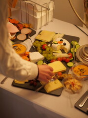 Hands preparing buffet table with fresh fruits and cheese platter
