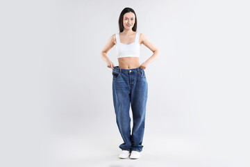 Woman wearing big jeans on light grey background
