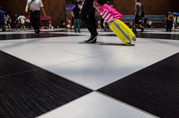 Fototapeta premium Traveler pulls bright yellow suitcase through airport terminal.