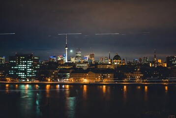 Fototapeta premium Panoramic view of berlin's illuminated skyline and tv tower reflecting on the spree river at night