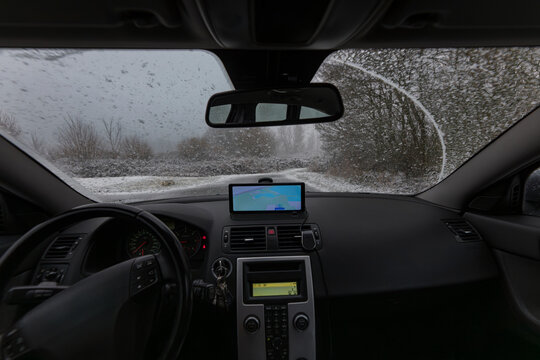 Driver point of view through windshield on snow-covered country road with GPS navigation mounted on dashboard during winter snowfall in the Netherlands