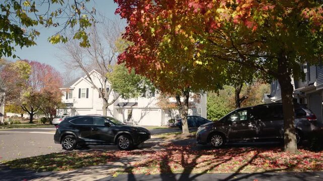 Quiet suburban neighborhood with parked cars and colorful autumn trees, peaceful residential street in fall season.