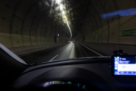 Driver perspective inside a highway tunnel with ceiling lights and car ahead showing red taillights with GPS navigation screen visible on dashboard