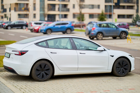 White electric car parked on city street with modern buildings in background. December 12, 2025 Brasov Romania