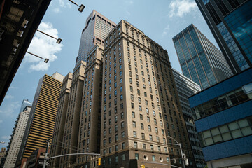 Naklejka premium A view from below shows a mix of historic brick buildings and modern glass towers in Midtown Manhattan. The bright sky and sharp angles highlight the city's diverse architecture.