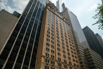 Obraz premium A row of towering skyscrapers rises high in Midtown Manhattan, New York City. The photo shows a mix of modern glass buildings and classic architecture under a bright sky.