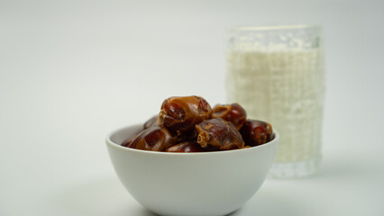 Obraz premium Bowl of fresh dates with glass of milk on white background